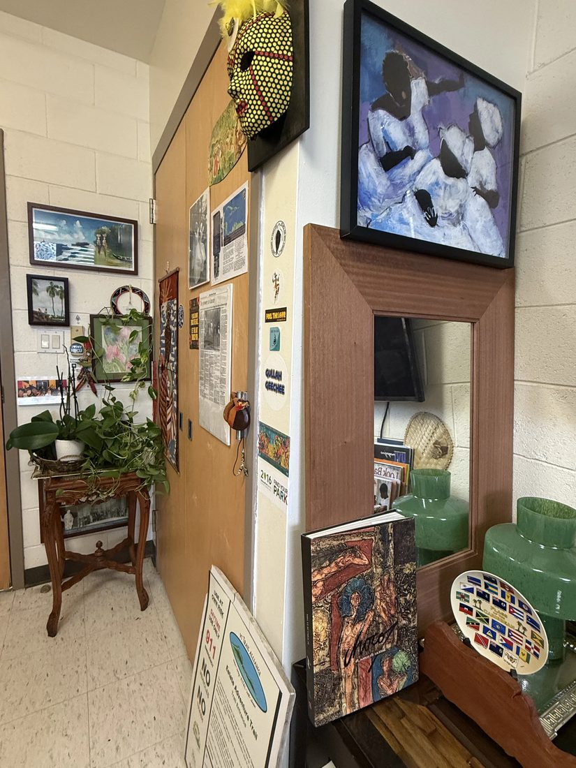 A corkboard display of community notices beside a framed painting of Caribbean dancers.