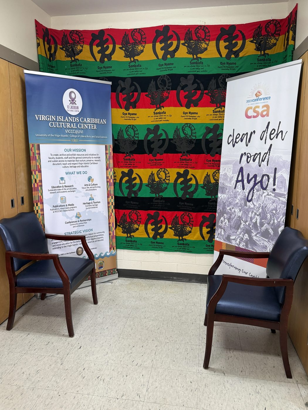 VICCC banners and a red, black, and green Adinkra-print cloth backdrop, flanked by two chairs, welcoming visitors to the center.