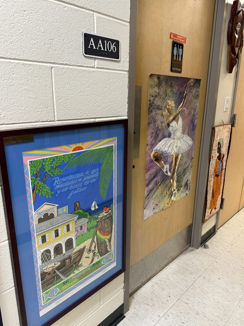 Framed Caribbean artwork, including a colorful folk painting, displayed in a hallway.
